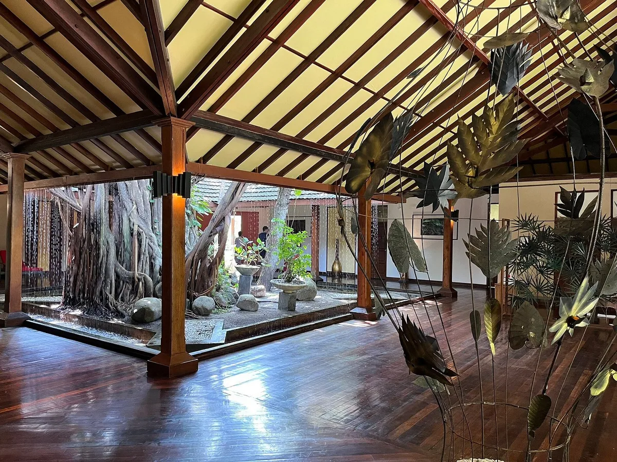 Adaaran Meedhupparu restaurant interior with wooden cathedral ceiling, central skylit banyan-tree courtyard, dark wood floor and metal palm-leaf sculptures, Raa Atoll, Maldives