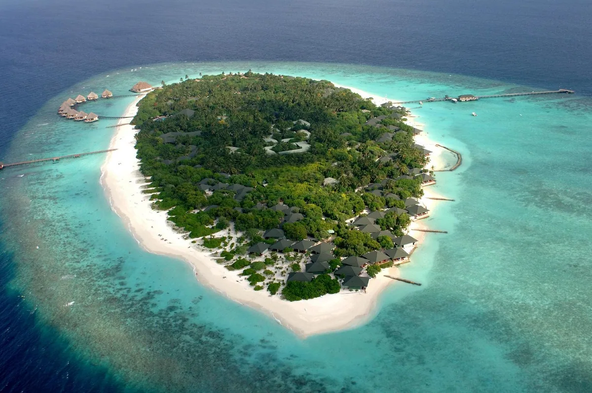 Adaaran Meedhupparu, wide aerial of Meedhupparu island with palm canopy, beach villa distribution and Prestige Water Villa cluster jetty on eastern reef edge, Raa Atoll, Maldives