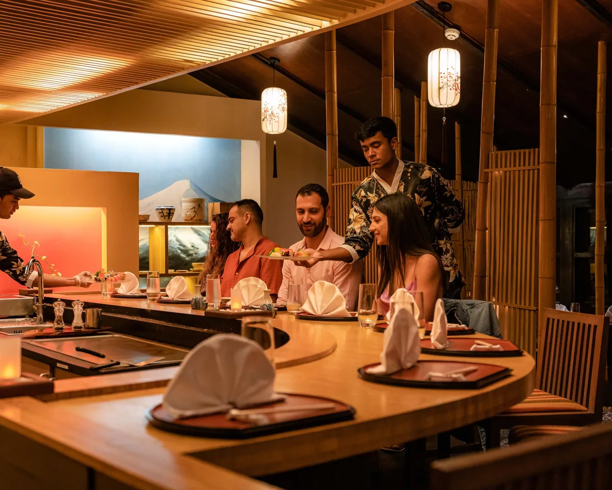 Adaaran Prestige Vadoo, dining, South Malé Atoll, Maldives, Kithajima Japanese restaurant interior, the bamboo-screen ceiling treatment, the Hokusai-wave Mt-Fuji backdrop, the U-shape sushi counter with chef preparing nigiri, and four guests around the counter watching the preparation (the property's standout standalone Japanese restaurant).