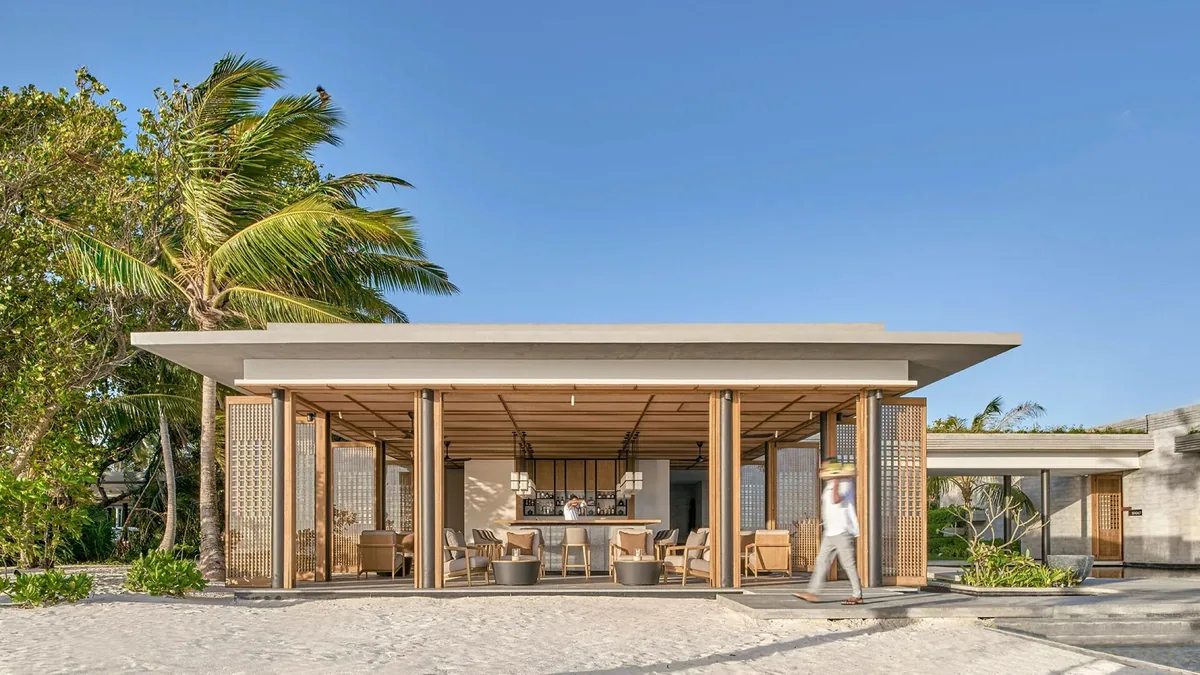 Alila Kothaifaru Maldives, Mirus Bar beachside flat-roof pavilion with wood-lattice screens, central bar and wooden tables on white sand, Raa Atoll, Maldives