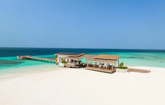 Alila Kothaifaru Maldives, The Shack daytime sandbank facility with solar-panel bar pavilion, lattice-roof dining area, jetty into lagoon and reef visible underwater, Raa Atoll, Maldives