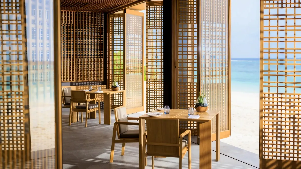 Alila Kothaifaru Maldives, Seasalt beachfront pavilion with Mashrabiya-style wood-lattice screens, wooden tables and chairs, open onto beach and turquoise ocean, Raa Atoll, Maldives