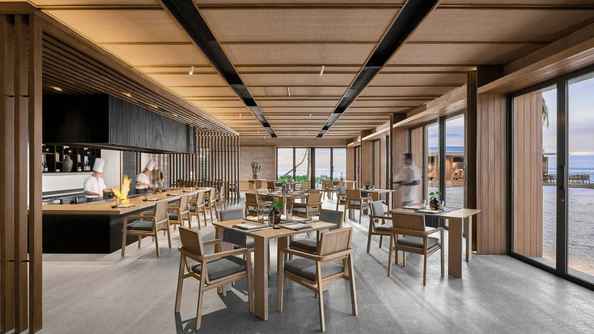 Alila Kothaifaru Maldives, Umami Japanese teppanyaki counter with chefs at flame grills, wooden ceiling with dark beams and glass walls onto beach, Raa Atoll, Maldives