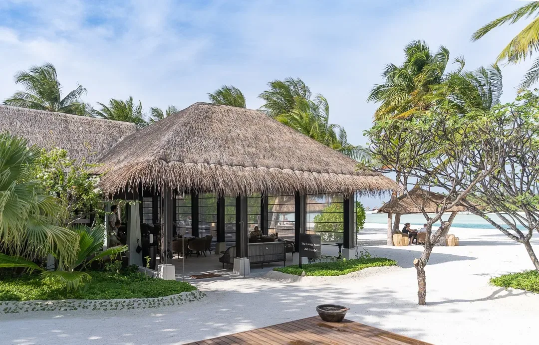 Naladhu Private Island Maldives, dining, South Malé Atoll, Maldives, Living Room standalone Naladhu venue, thatched pavilion under the palm canopy with raised timber deck, white sands surrounding the entry steps and the palm-frond canopy reaching down to the eaves.