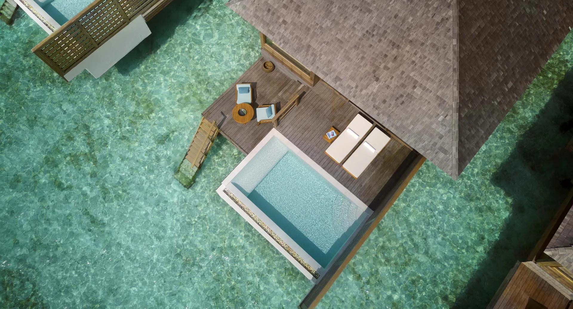Anantara Veli Maldives Resort, villa overwater, South Malé Atoll, Maldives, Over Water Pool Villa top-down aerial, single villa with rectangular private pool on the dark-stained deck, thatched roof and the lagoon sand-and-coral pattern visible through the water below.