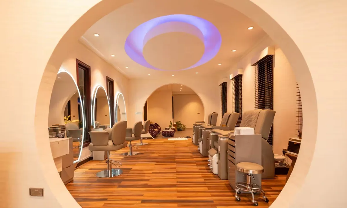Atmosphere Kanifushi Maldives, spa, Lhaviyani Atoll, Maldives, Essens Spa salon framed by a circular archway entry, oval ring mirrors at the styling stations, pedicure chairs, and a blue-lit ceiling oculus.