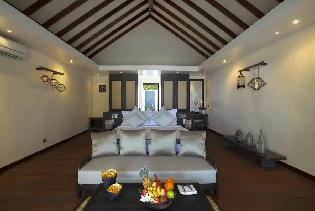 Atmosphere Kanifushi Maldives, villa beach, Lhaviyani Atoll, Maldives, Beach Pool Villa interior with vaulted exposed-beam ceiling, diamond-cage wire pendant sconces, and private garden door beyond the king bed.