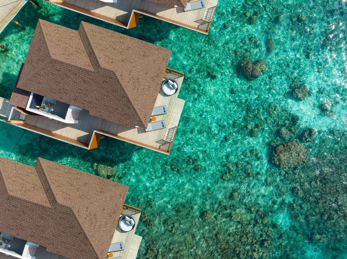 Avani+ Fares Maldives, top-down aerial of water villa row with pitched shingle roofs and circular plunge pools on lagoon decks, Baa Atoll, Maldives