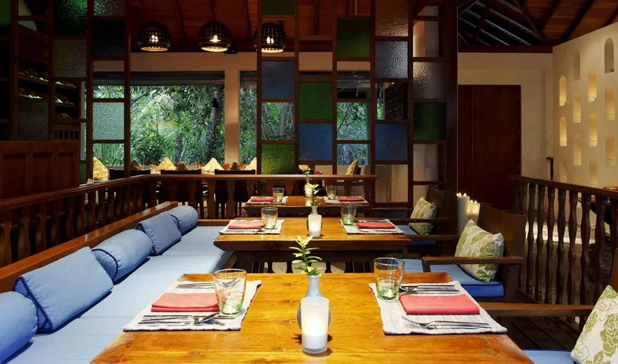 Centara Grand Island Resort & Spa Maldives, dining, Alif Dhaal (South Ari) Atoll, Maldives, Suan Bua Thai restaurant interior with the dark-wood pavilion roof, a multi-color glass-mosaic feature wall (blue, green, orange tiles in a grid), low-banquette tables with red placemats and pale-blue cushions, drum-shaped raffia pendant lights overhead.