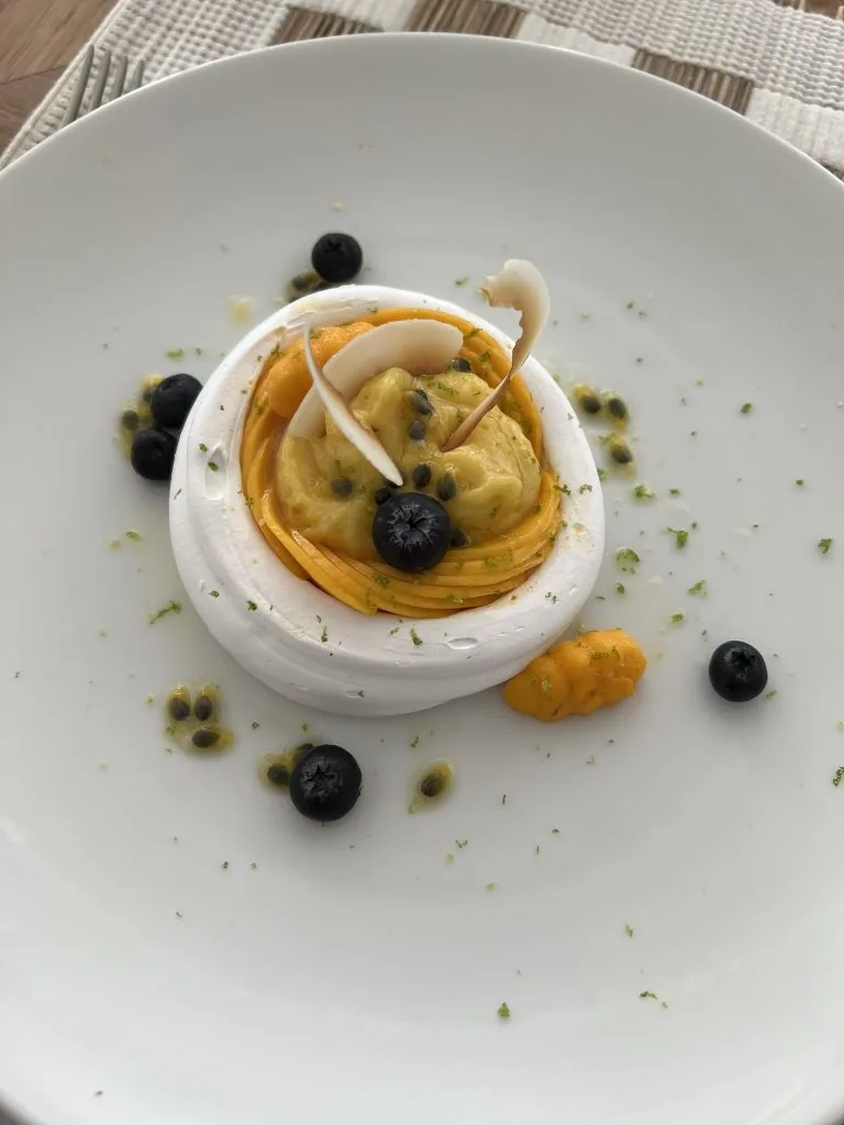 COMO Cocoa Island, dining, South Malé Atoll, Maldives, COMO Shambhala plated dessert at Ufaa, mango-coulis spiral wrapped around lemon-cream centre, white-chocolate shard and blueberries scattered with passion-fruit pulp and lime zest across the white plate.