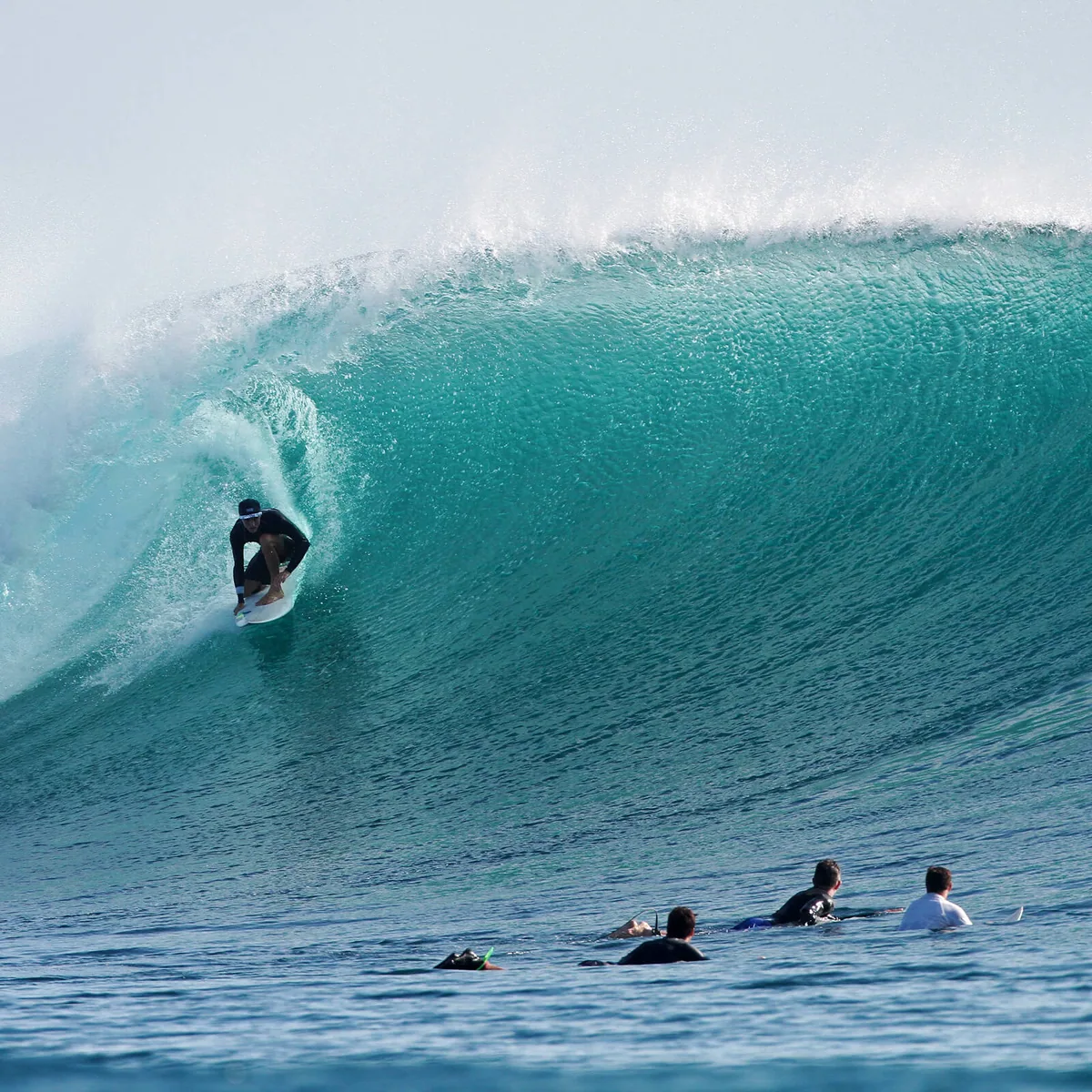 COMO Maalifushi, activity, Thaa Atoll, Maldives, Maalifushi surf break, a surfer riding inside a curling barrel wave at the property's dedicated surf-break programme (Thaa Atoll's signature break), other surfers waiting in the line-up in the foreground.