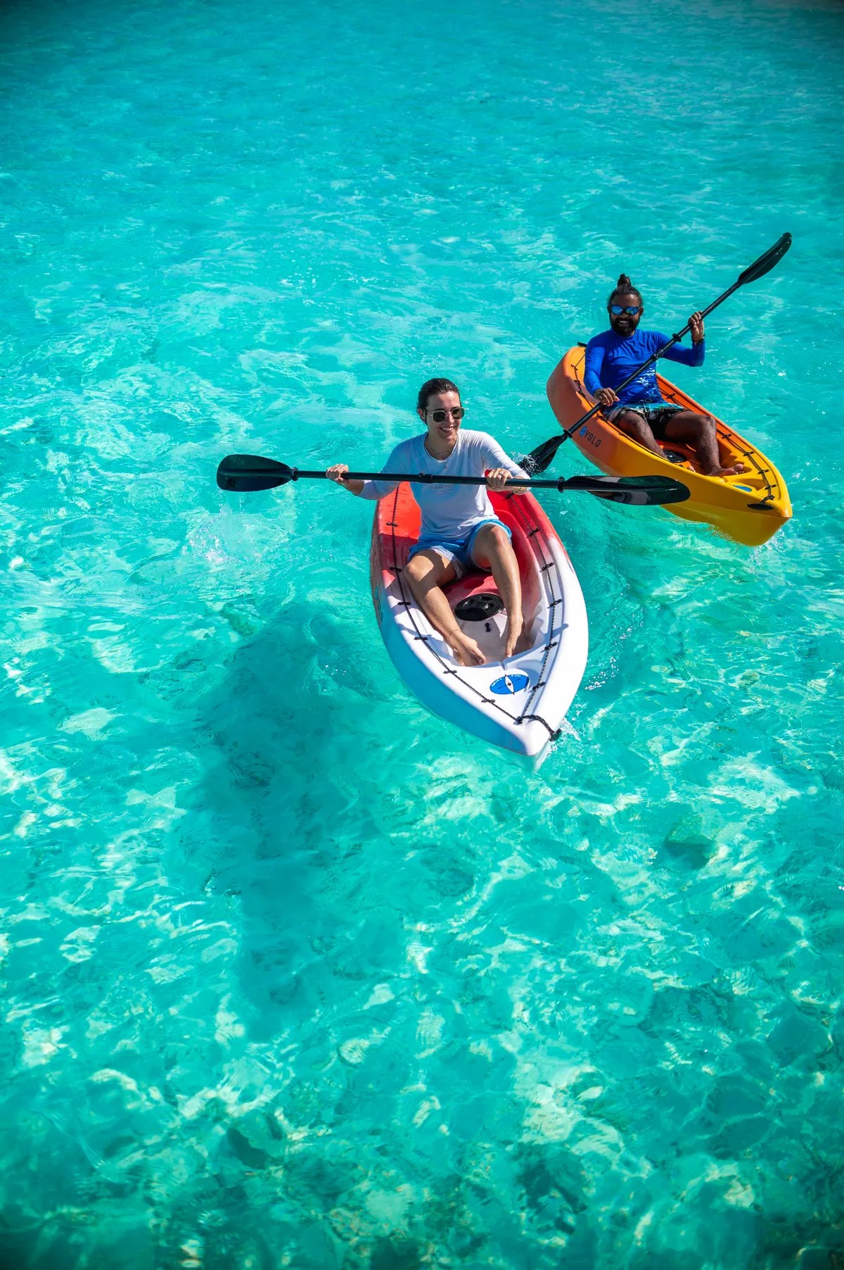 Diamonds Thudufushi Beach & Water Villas, activities, Alif Dhaal (South Ari) Atoll, Maldives, Two kayakers crossing the shallow turquoise Thudufushi lagoon in red and yellow kayaks, the clear water revealing the sand-and-reef texture beneath, the dive-and-watersports programme on the South Ari Atoll edge.