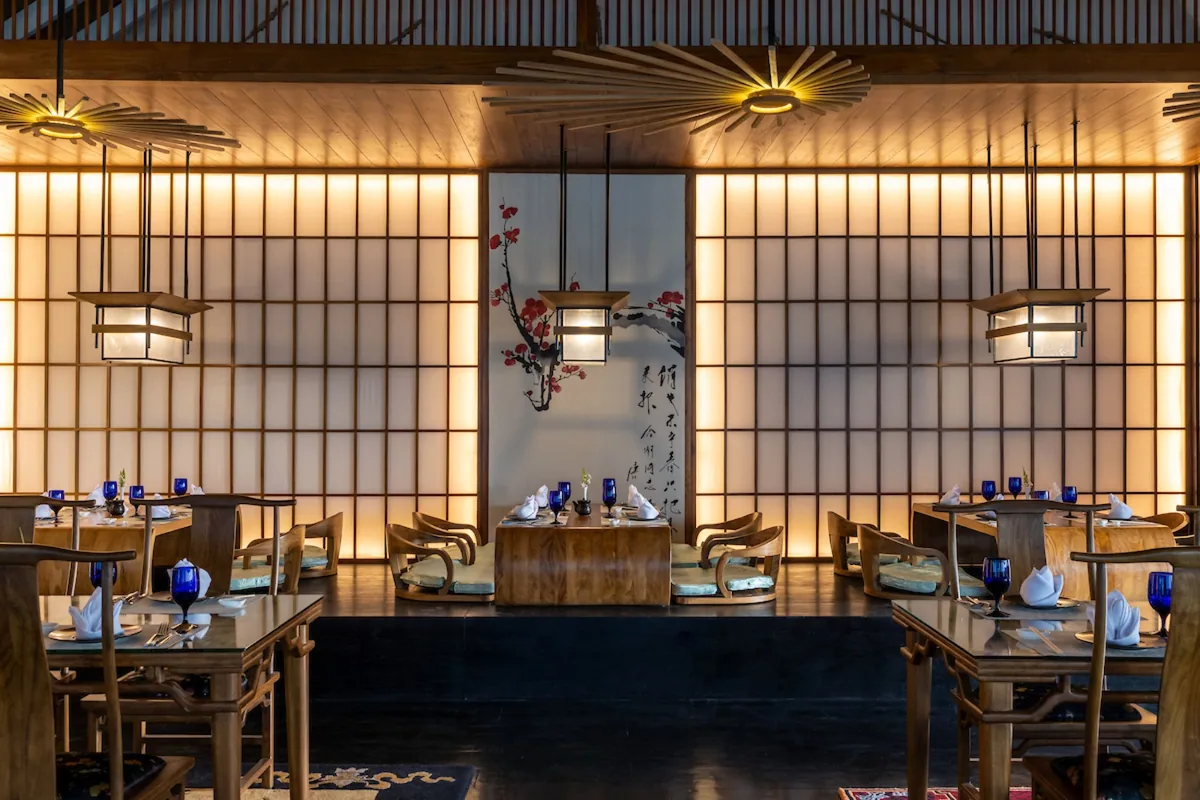 Emerald Faarufushi, Le Asiatique Asian-Japanese interior with backlit shoji screens, fan-shape hanging lamps, calligraphy + cherry-blossom wall art and dark wood tables with blue glassware, Raa Atoll, Maldives