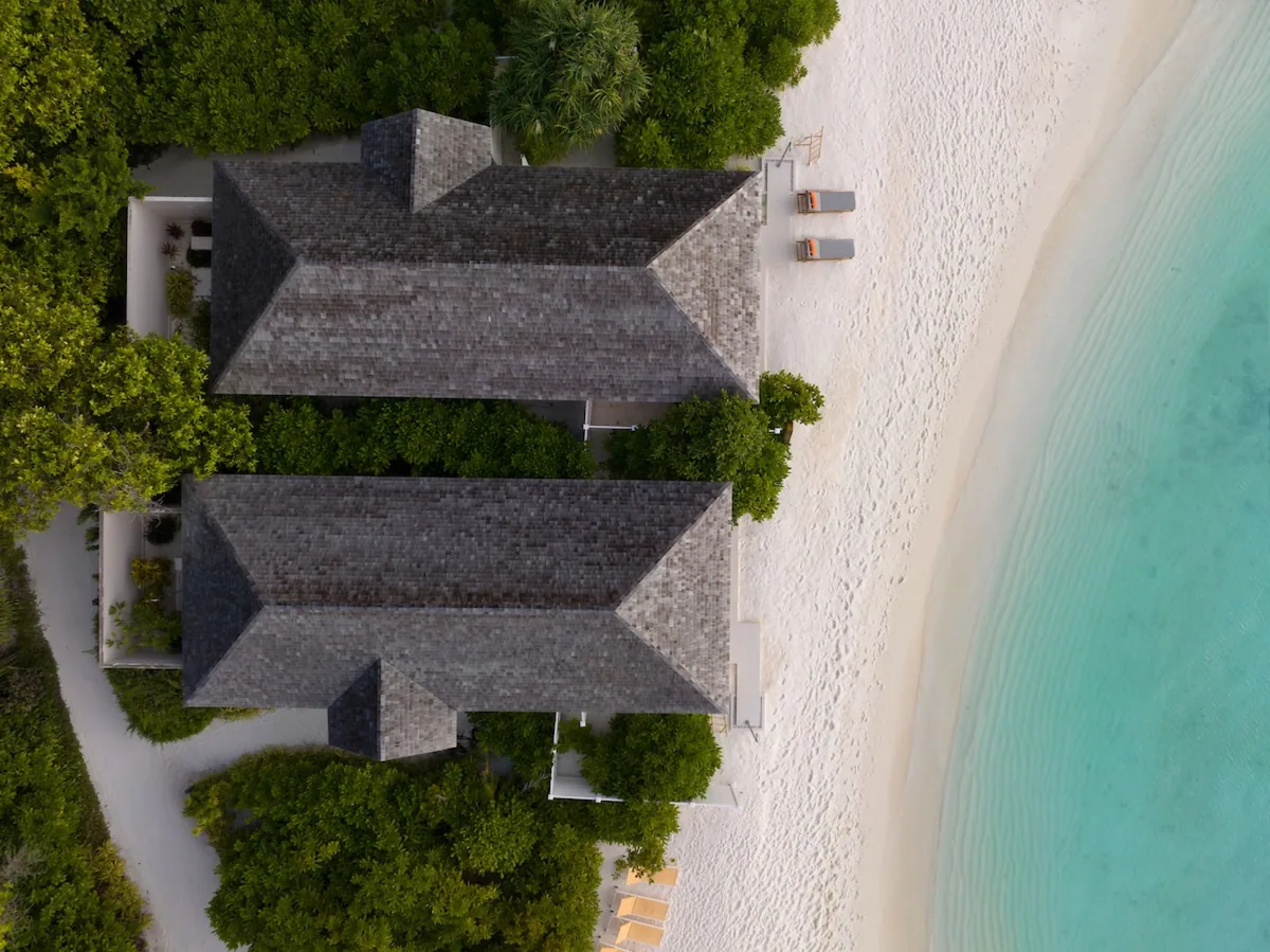 Emerald Faarufushi, top-down aerial of beach villa rooftops with shingle-tile geometric pattern, sand, palm canopy and lagoon edge, Raa Atoll, Maldives