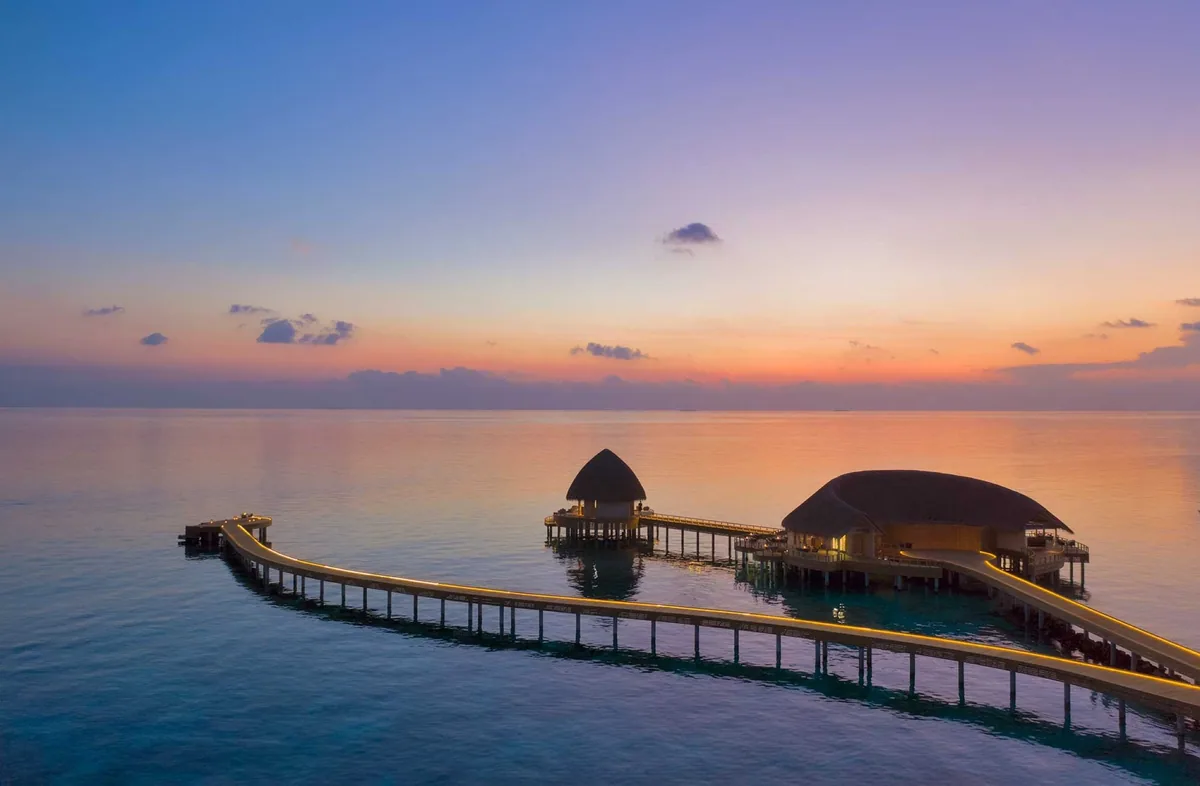 Emerald Faarufushi, Mediterraneo at sunset with thatched-roof pavilion at jetty end, LED strip lighting, sundowner gazebo, pink-peach sunset sky, Raa Atoll, Maldives