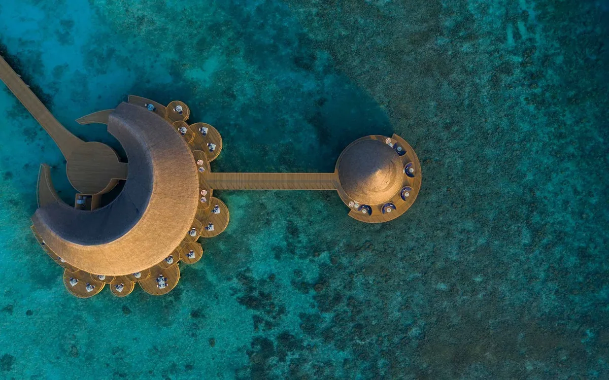 Emerald Faarufushi, Mediterraneo overwater Italian restaurant top-down aerial showing crescent-shape thatched roof with circular dining bumps + jetty + sundowner gazebo over turquoise reef, Raa Atoll, Maldives