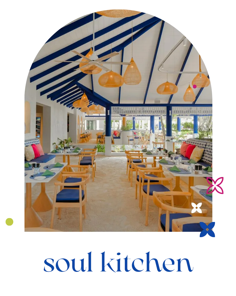 Eri Maldives, dining, North Malé Atoll, Maldives, Soul Kitchen restaurant interior (Eri Maldives rebrand): Mediterranean-coastal palette with a blue-and-white striped peaked-canvas ceiling, hanging woven orange and yellow rattan pendant lights, blonde-wood dining tables and chairs with blue cushion accents, sand-coloured floor under the bright pavilion.