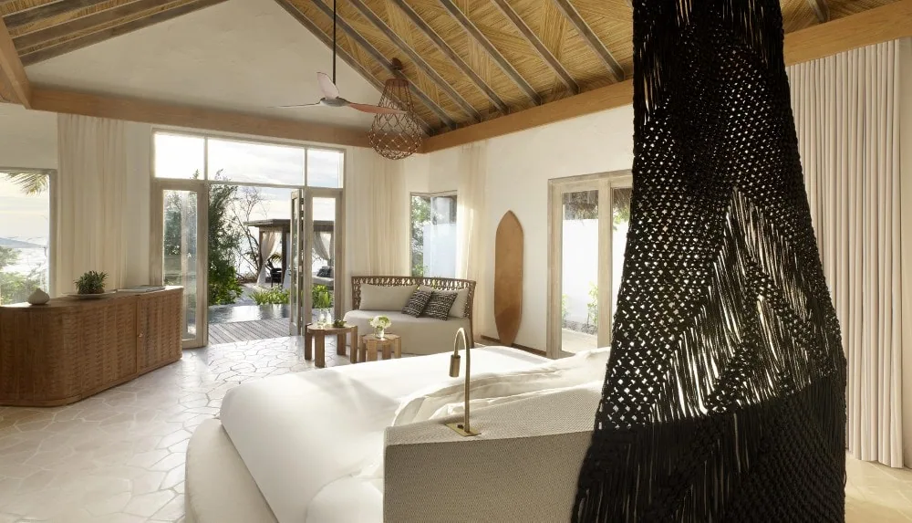 Sirru Fen Fushi Private Lagoon Resort, Beach Sunset Pool Villa interior with macrame bed canopy, palm-thatched cathedral ceiling, rattan console, terrazzo floor and wooden surfboard feature, Shaviyani Atoll, Maldives