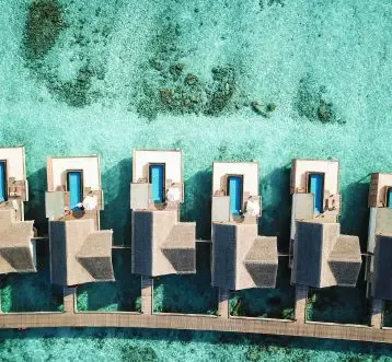 Sirru Fen Fushi Private Lagoon Resort, top-down aerial of water villa cluster with private plunge pools, slate-tile rooftops and jetty arm along reef shelf, Shaviyani Atoll, Maldives