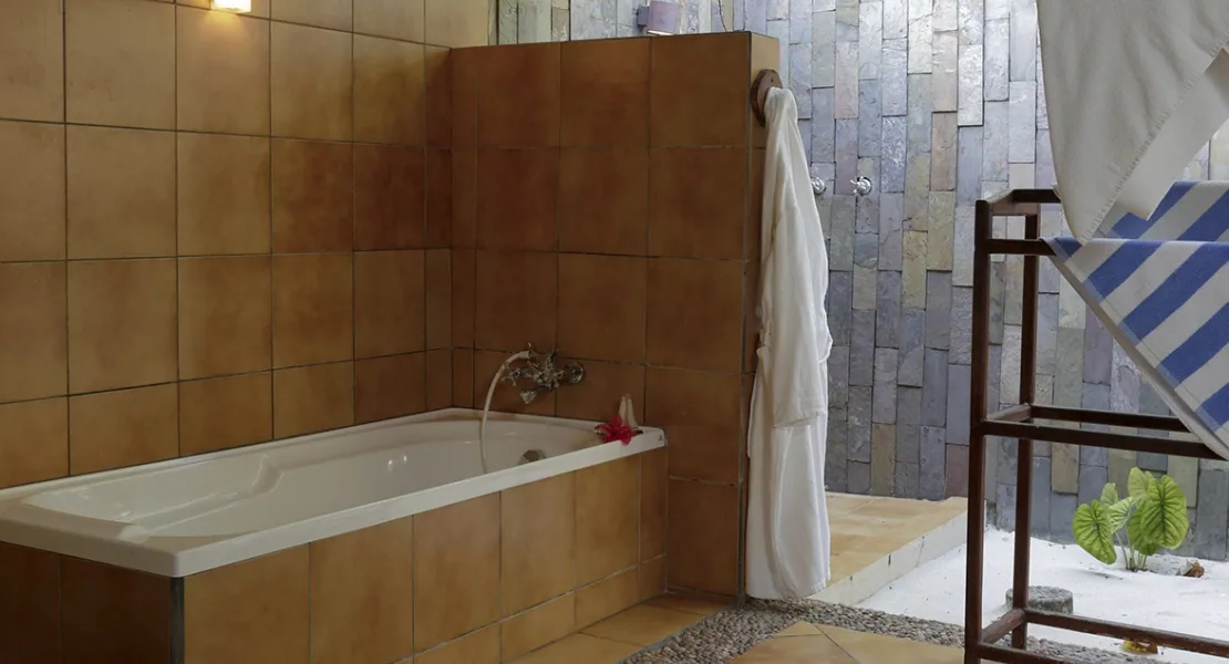 Filitheyo Island Resort, villa interior, Faafu Atoll, Maldives, Deluxe Villa open-air bathroom, terracotta-tiled bathtub set against a slate-tile feature wall, white robe on wooden rack at the outdoor shower hardscape, gravel-and-plant garden floor.