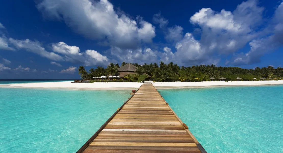 Filitheyo Island Resort, setting, Faafu Atoll, Maldives, Signature wooden jetty arrival approaching the palm-covered Filitheyo island with thatch-roofed pavilion at the far end, the property's primary arrival composition in central Faafu Atoll.