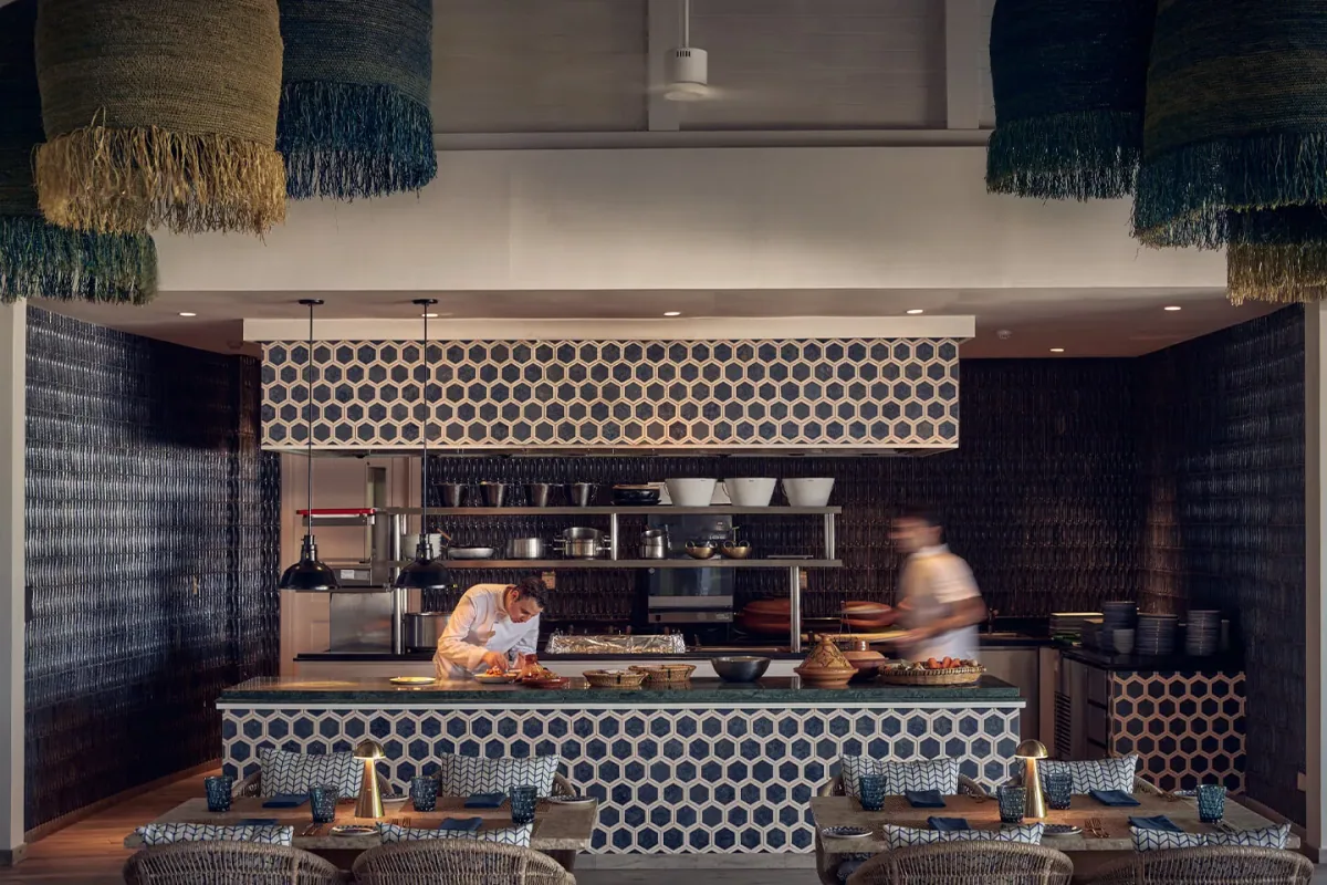 Finolhu Baa Atoll, dining, Baa Atoll, Maldives, Arabian Grill open kitchen, the hexagonal-tile chef station with the cooks working the grill, deep-blue patterned chairs at the counter and the hanging green-tassel macrame curtains framing the bar entry.
