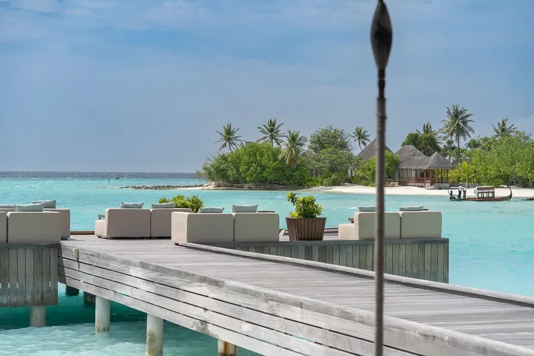 Four Seasons Resort Maldives at Kuda Huraa, spa, North Malé Atoll, Maldives, Spa Island viewed across the lagoon from the Sunset Bar deck, the islet's thatched treatment pavilions sitting under palm shade, traditional dhoni pulled up on the white-sand crescent at the islet's edge.