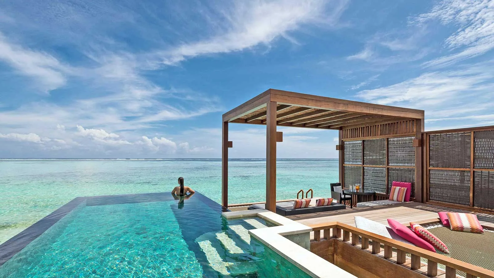 Four Seasons Resort Maldives at Kuda Huraa, villa overwater, North Malé Atoll, Maldives, Sunrise Water Villa deck, the timber pergola shading the infinity-edge plunge pool and the magenta-cushion daybed running the lagoon side.