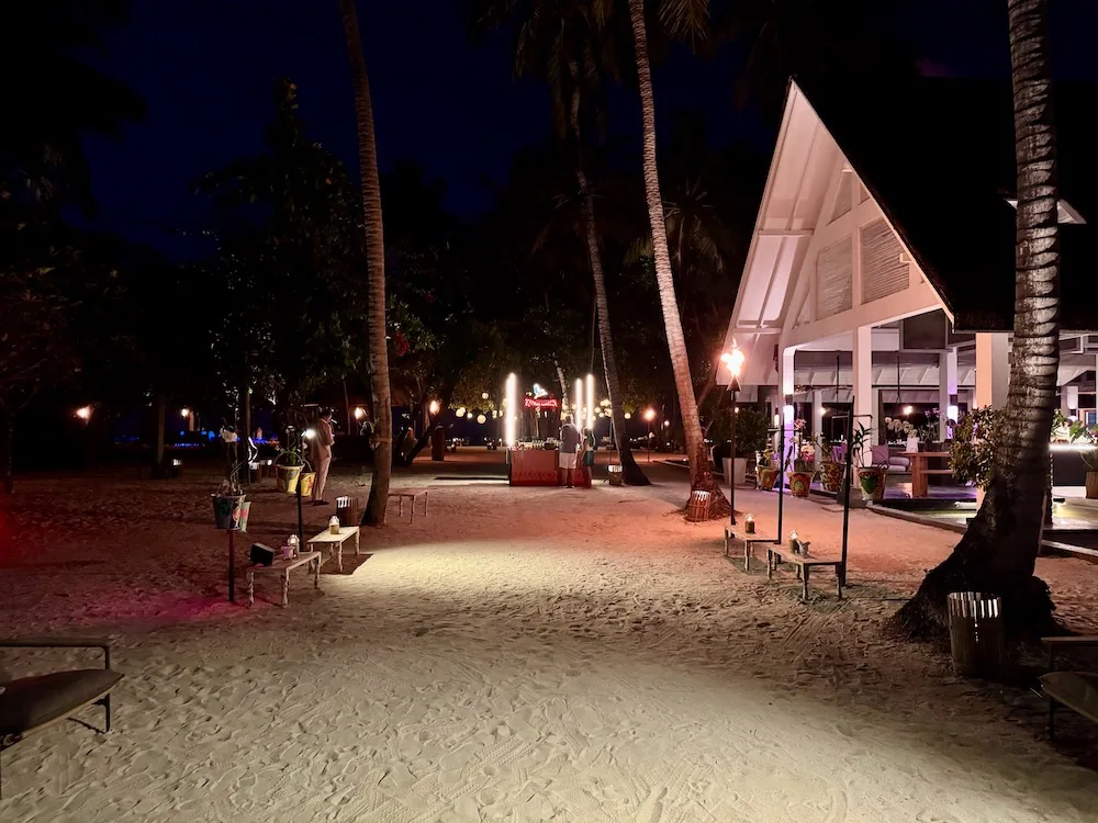Four Seasons Resort Maldives at Landaa Giraavaru, dining, Baa Atoll, Maldives, Cafe Landaa, the white A-frame all-day pavilion lit at night, a sand-floor courtyard arranged with low candle-stand benches and a market-style live station.