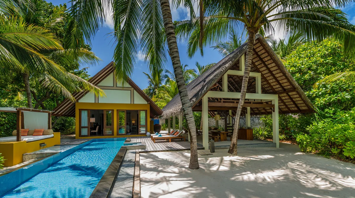 Four Seasons Resort Maldives at Landaa Giraavaru, villa beach, Baa Atoll, Maldives, Family Beach Bungalow with private pool, a thatched-roof structure with covered terrace and yellow-walled vestibule glimpsed through the open doorway, dense palm canopy at the natural-island interior.