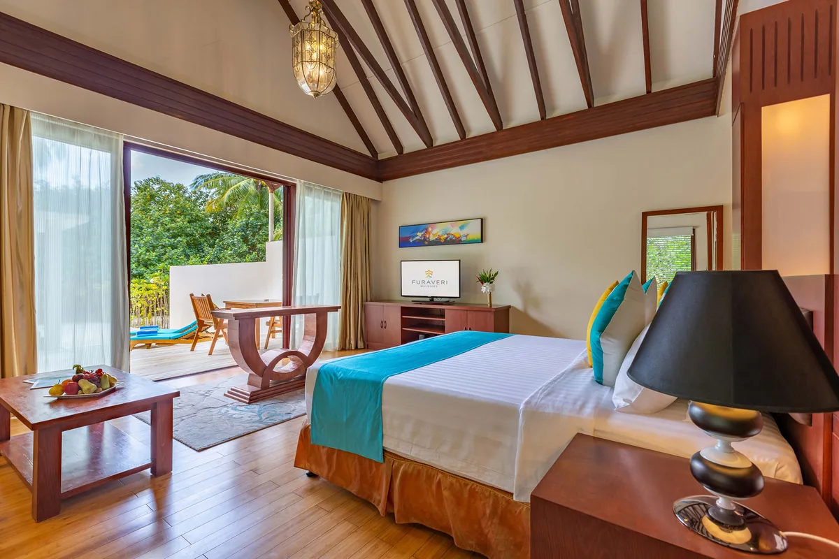 Furaveri Maldives, Garden Villa interior with cathedral white ceiling, dark wood beams, lantern pendant, king bed with multi-colour cushions and TV displaying Furaveri logo, Raa Atoll, Maldives