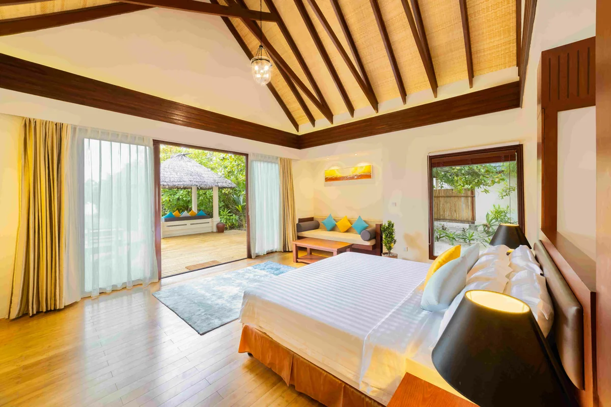 Furaveri Maldives, Beach Villa interior with palm-leaf woven cathedral ceiling, king bed, yellow curtains and glass doors to thatched daybed terrace, Raa Atoll, Maldives