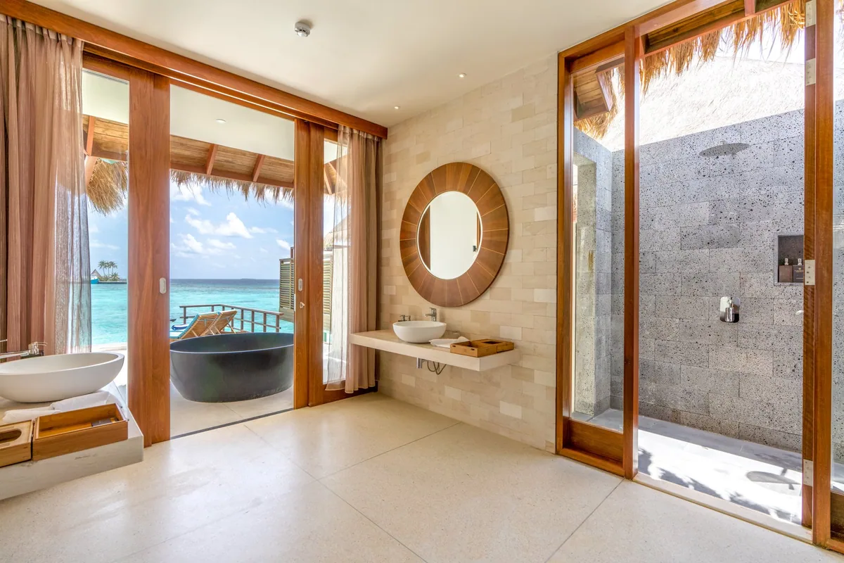 Furaveri Maldives, Ocean Pool Villa bathroom with twin vessel sinks, round mirror, stone-tile walls, freestanding black bathtub on terrace facing lagoon and stone shower, Raa Atoll, Maldives