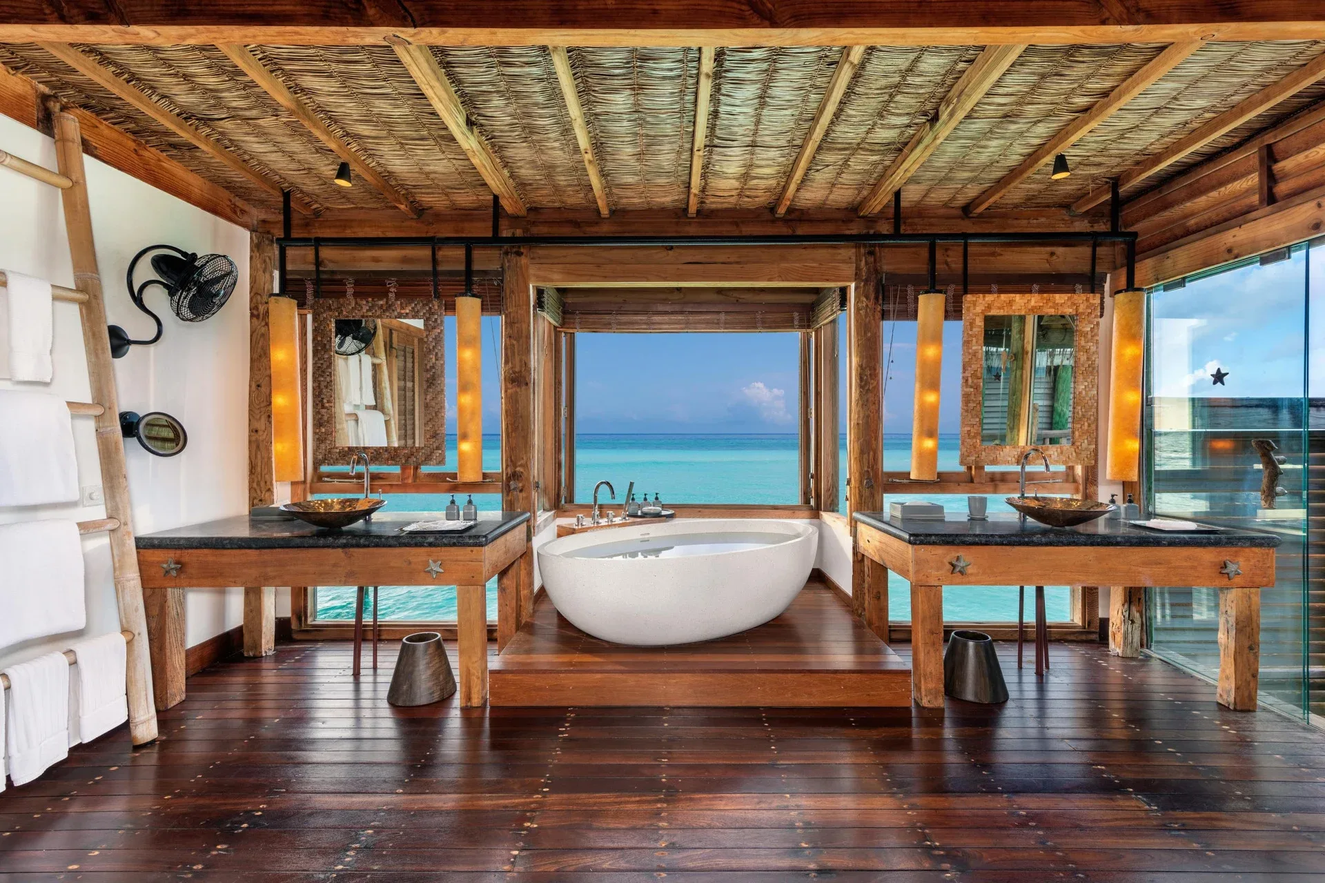 Gili Lankanfushi, villa overwater, North Malé Atoll, Maldives, Villa bathroom: twin reclaimed-timber vanities flanking a freestanding white oval bathtub centred against a picture window opening onto the lagoon, vaulted bamboo ceiling.