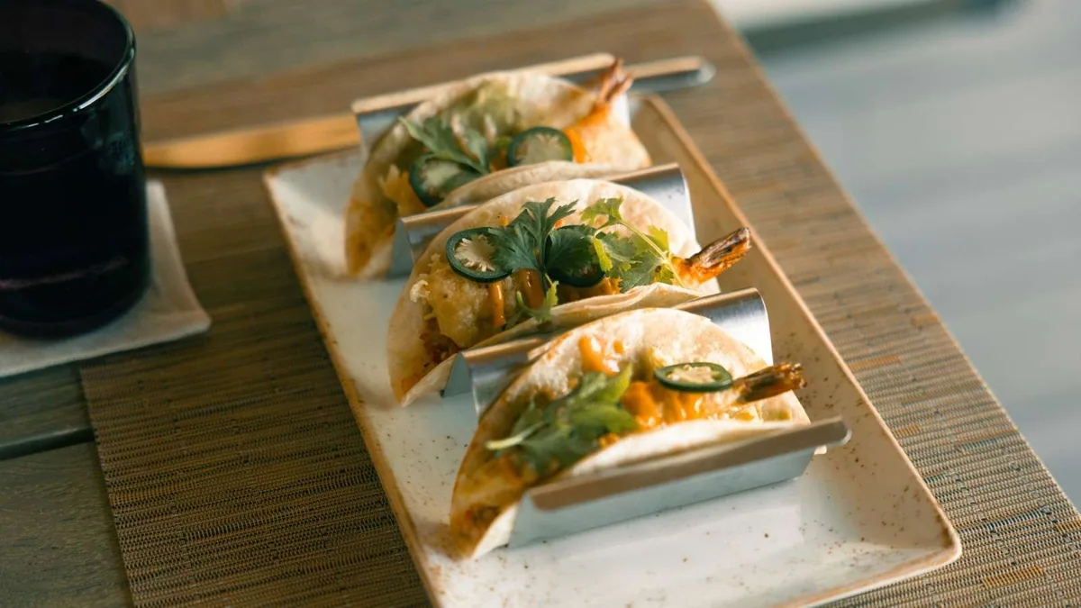 Hurawalhi Island Resort, dining, Lhaviyani Atoll, Maldives, JFK (Junk Food Kitchen) shrimp tacos plated on a ceramic platter with cilantro, jalapeno and creamy sauce on a woven placemat.