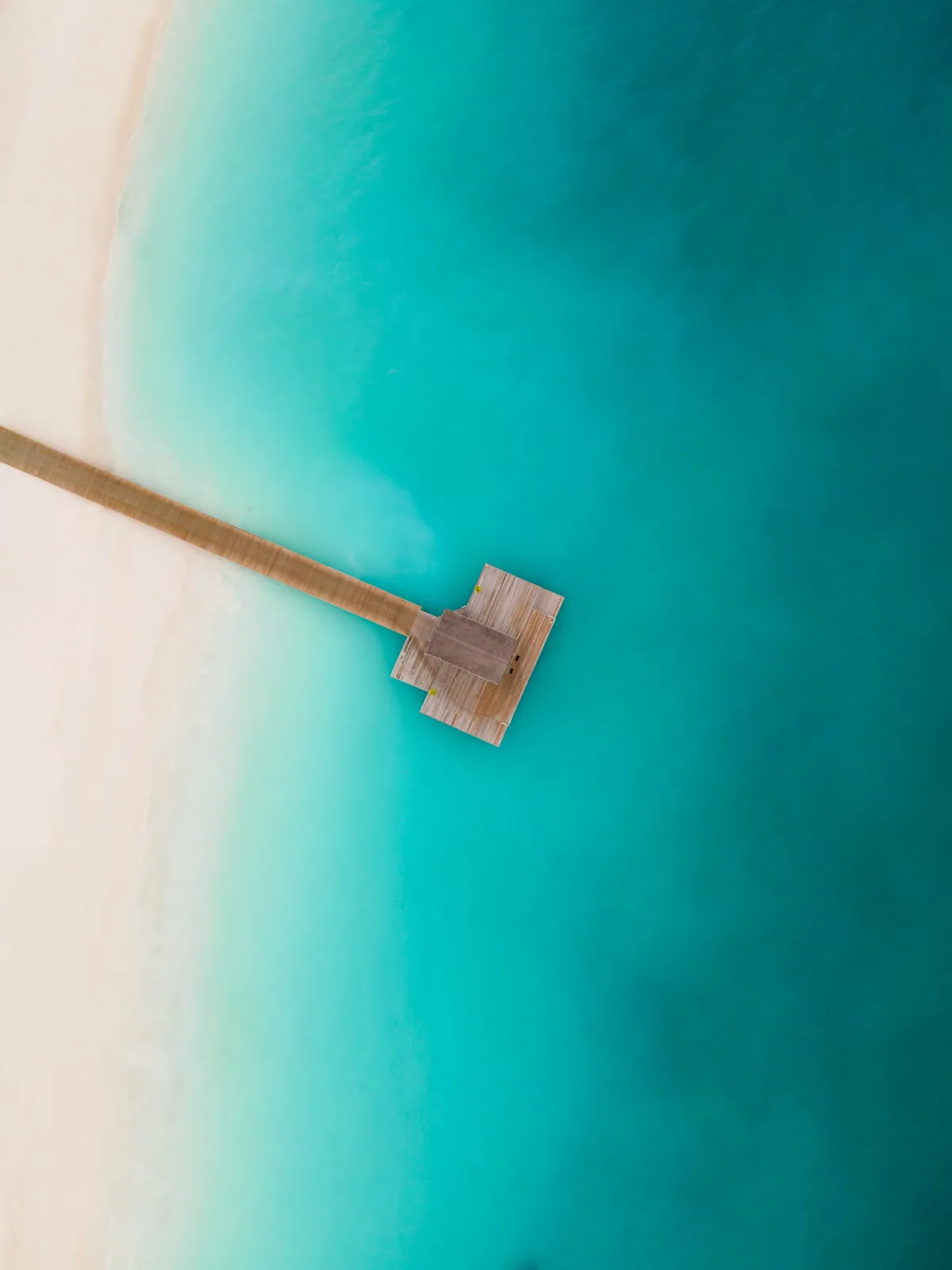 Sun Siyam Iru Veli, aerial, Dhaalu Atoll, Maldives, Top-down aerial of the property's arrival jetty, a long timber walkway extending from the white-sand Maaenboodhoo beach into the lagoon, landing pavilion at the jetty terminus, reef gradient from white-sand shallows to deep turquoise.