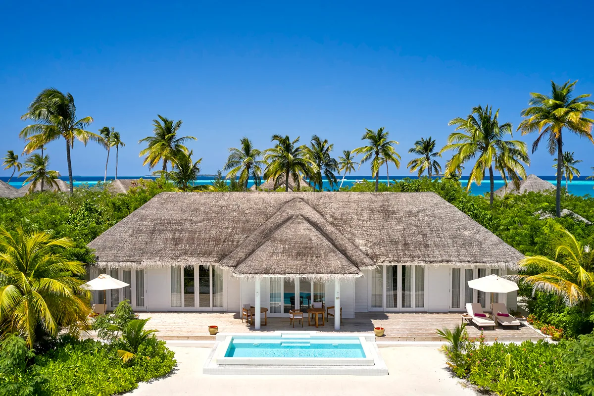 Sun Siyam Iru Veli, villa beach, Dhaalu Atoll, Maldives, Two-Bedroom Beach Pool Villa from above, a symmetric triple-thatched-peak pavilion fronted by a private rectangular pool, twin sets of sun loungers under matching umbrellas, dense palm canopy framing both wings, white-sand beach beyond.