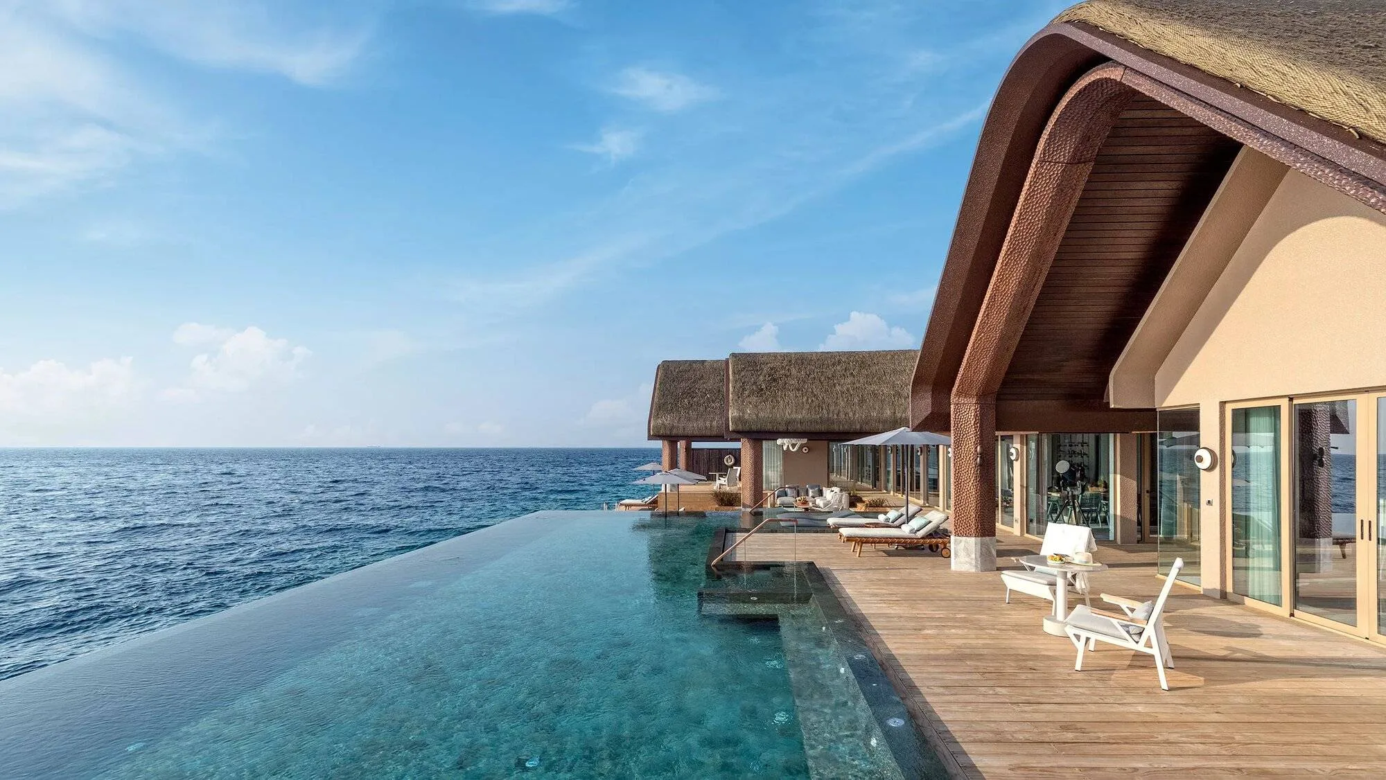 JOALI BEING, villa overwater, Raa Atoll, Maldives, Four-Bedroom Wellbeing Private Ocean Residence sundeck, the curved bronze-clad arch beams that define JOALI BEING's signature architectural register, infinity pool stretching toward the horizon.