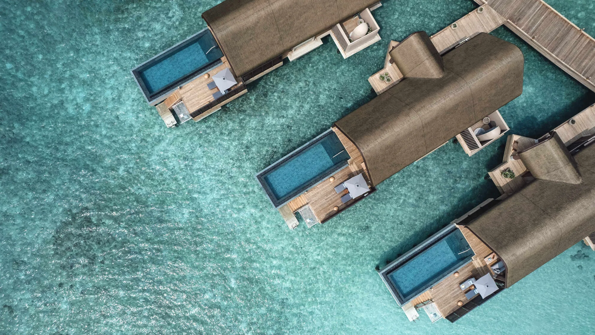 JOALI BEING, villa overwater, Raa Atoll, Maldives, Ocean Pool Villa cluster, top-down aerial of three over-water villas with rectangular private pools on each deck, the signature thatched-roof Studio Apostroph architecture.