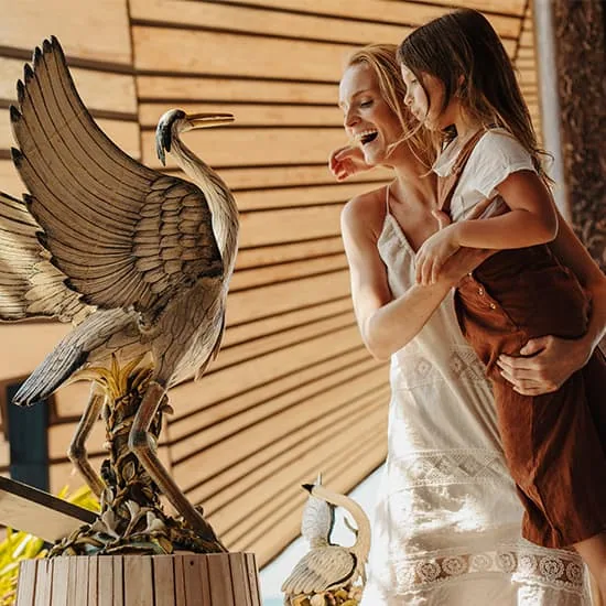 JOALI Maldives, art tour, Raa Atoll, Maldives, Curator-led art tour engagement: a mother and daughter at one of the bronze heron sculptures inside the Vandhoo pavilion (horizontal-slat timber walls), part of the 30+ site-specific commissioned works on the JOALI artscape walk.