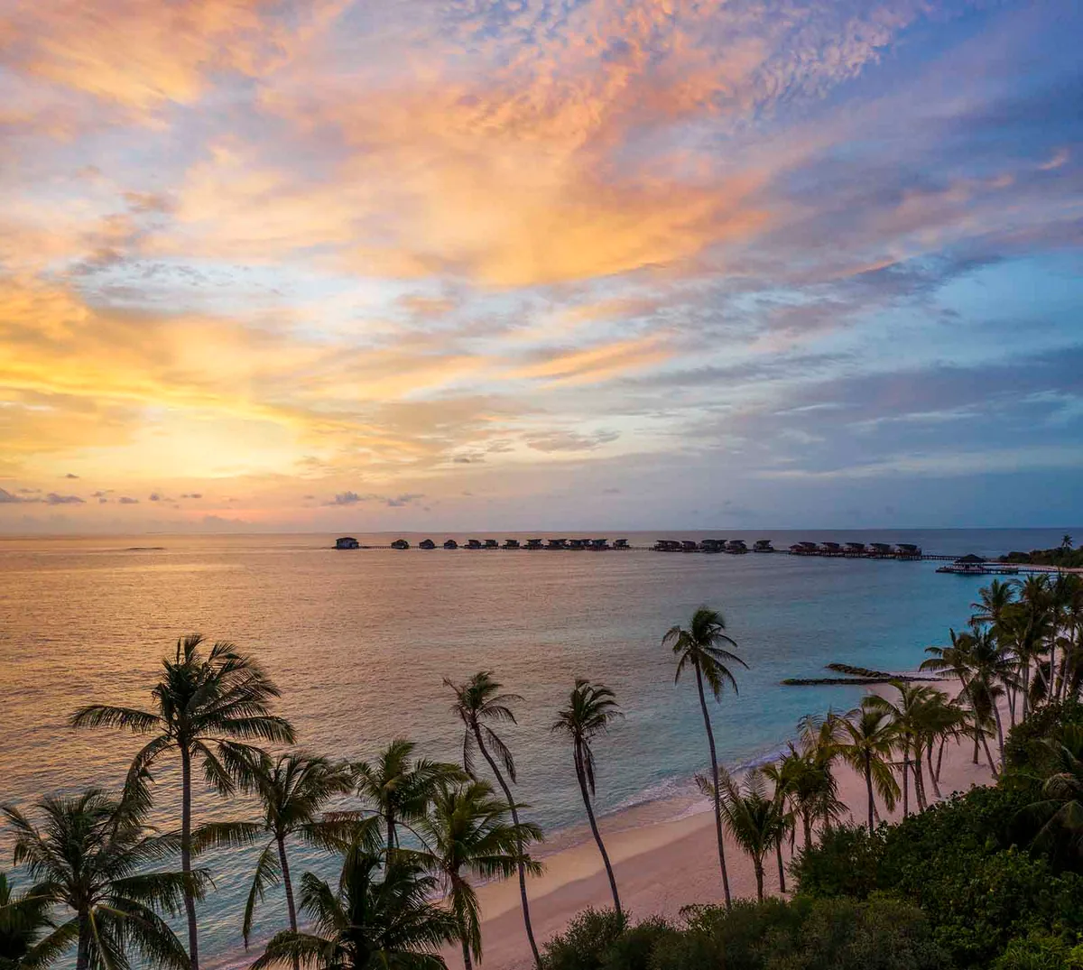 JW Marriott Maldives Resort & Spa, Vagaru sunset aerial with palm canopy and overwater villa silhouette, Shaviyani Atoll, Maldives