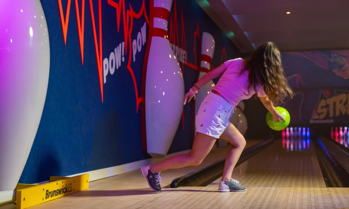 Kandima Maldives, activity, Dhaalu Atoll, Maldives, PlaySpace bowling alley, neon-comic-pop wall art with the words POW and STRIKE, oversized bowling-pin sculptures as decor, a player mid-throw with a green ball heading down the lane (a recent addition to the property's activities).