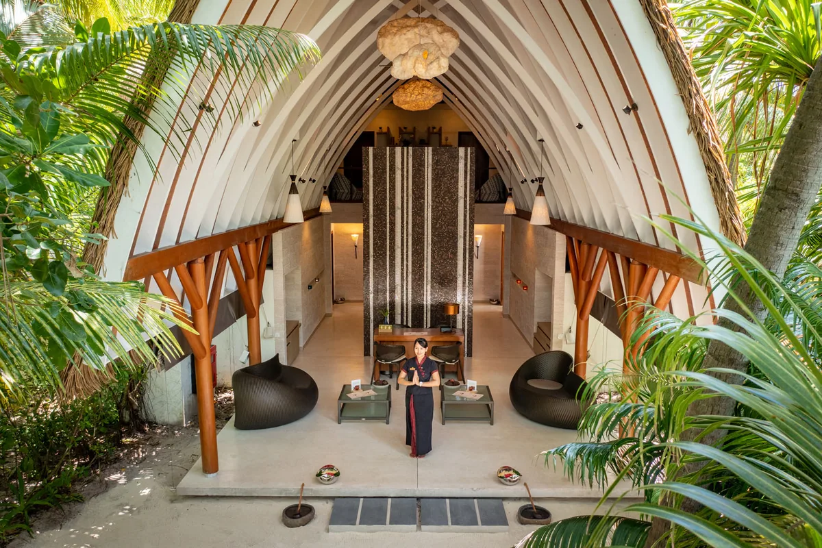 Kandolhu Maldives, spa, Alif Alif Atoll (North Ari), Maldives, Varu Spa entrance pavilion, dramatic cathedral-form curved timber-rafter peaked vault soaring overhead, sculptural water-feature at the centre and a fan-shaped pendant chandelier descending from the apex. One of the country's most architecturally distinctive spa pavilions.