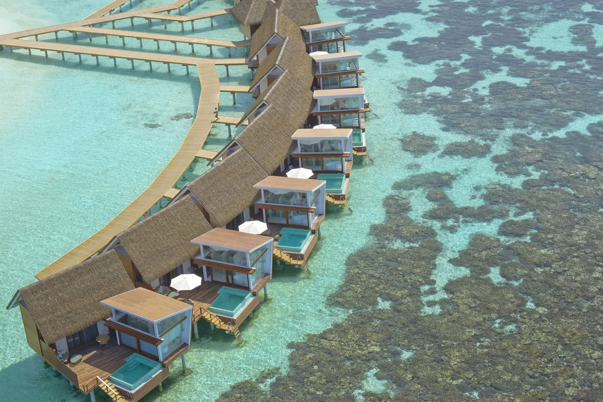 Kandolhu Maldives, setting, Alif Alif Atoll (North Ari), Maldives, Ocean Villa row aerial with the coral reef visible directly below the overwater villas, the property's house-reef-from-overwater-villa identity at its strongest. Kandolhu's siting on the coral pinnacle is structurally distinctive across the country.