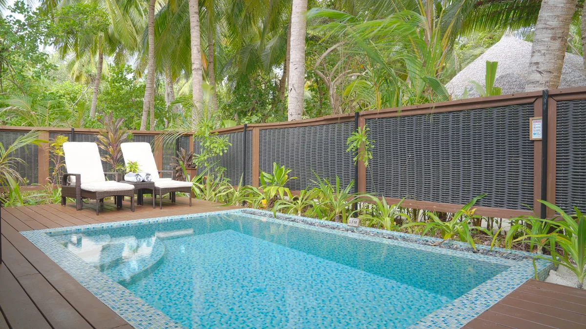 Kihaa Maldives, villa beach, Baa Atoll, Maldives, Garden Villa private pool deck, the mosaic-tile rectangular pool with twin cream-cushioned sun-loungers on the timber decking, hand-cut woven-bamboo privacy screen to the side and the dense palm-and-tropical-foliage canopy enclosing the deck.