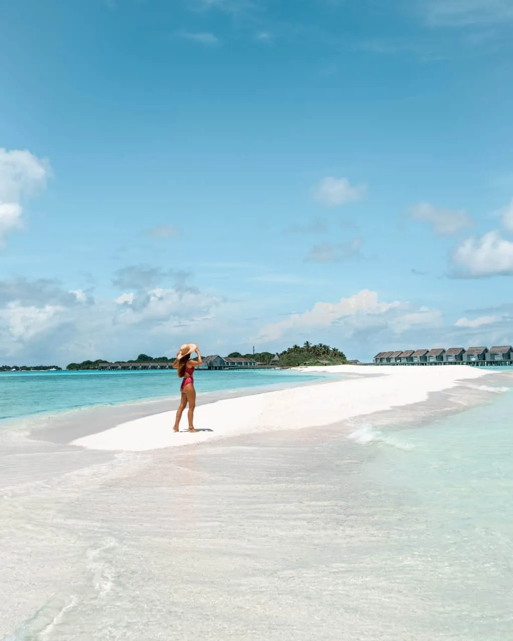 Niva Kuramathi Maldives (formerly Kuramathi Maldives), setting, Alif Alif Atoll (North Ari), Maldives, The iconic Kuramathi sandbank tip, white-sand strip extending into the turquoise lagoon with a figure in the middle distance, brown-roof Water Villa row visible on the right and the palm-covered main island catching the horizon. The property's most-photographed geographic feature.