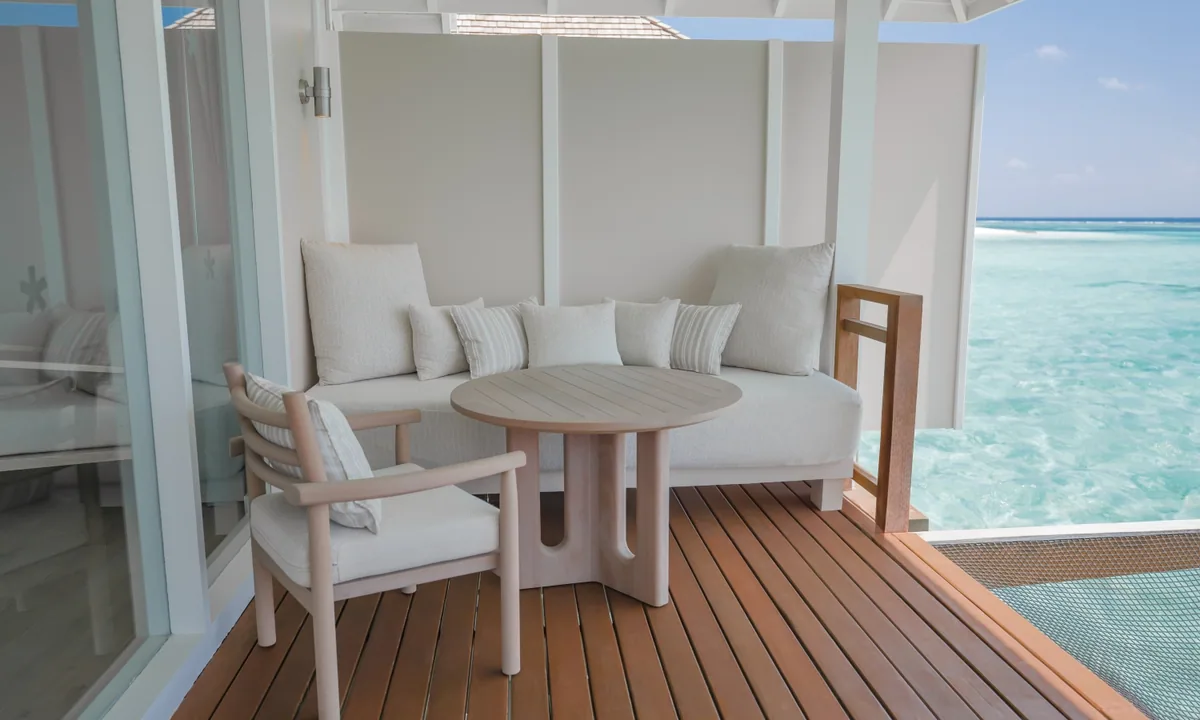 LUX* South Ari Atoll, villa overwater, Alif Dhaal (South Ari) Atoll, Maldives, Refurbished Water Villa private deck with the bleached-teak floor, pale-linen built-in banquette, light-wood round table, and the infinity-line lagoon view onto the reef edge.