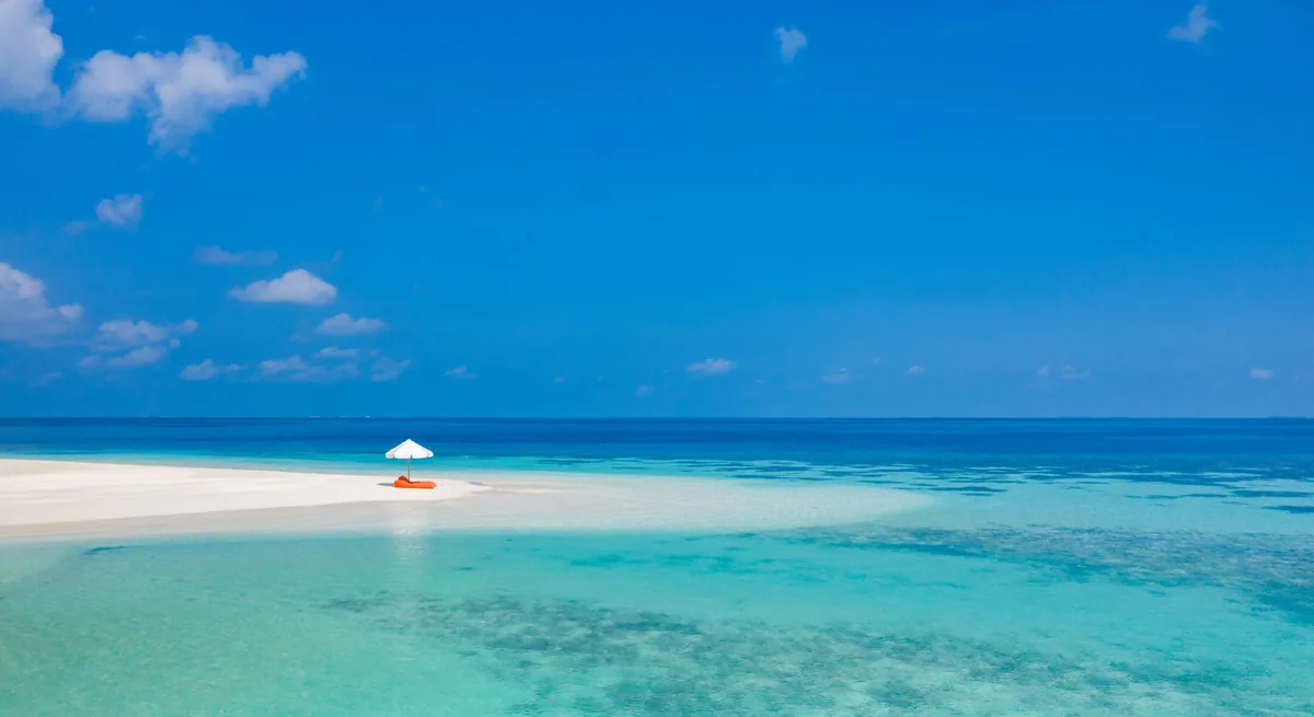 Mirihi Island Resort, setting, Alif Dhaal (South Ari) Atoll, Maldives, Sandbank picnic excursion setup with the solo white parasol and red lounger on a sand spit and the reef pattern visible in the surrounding shallows.
