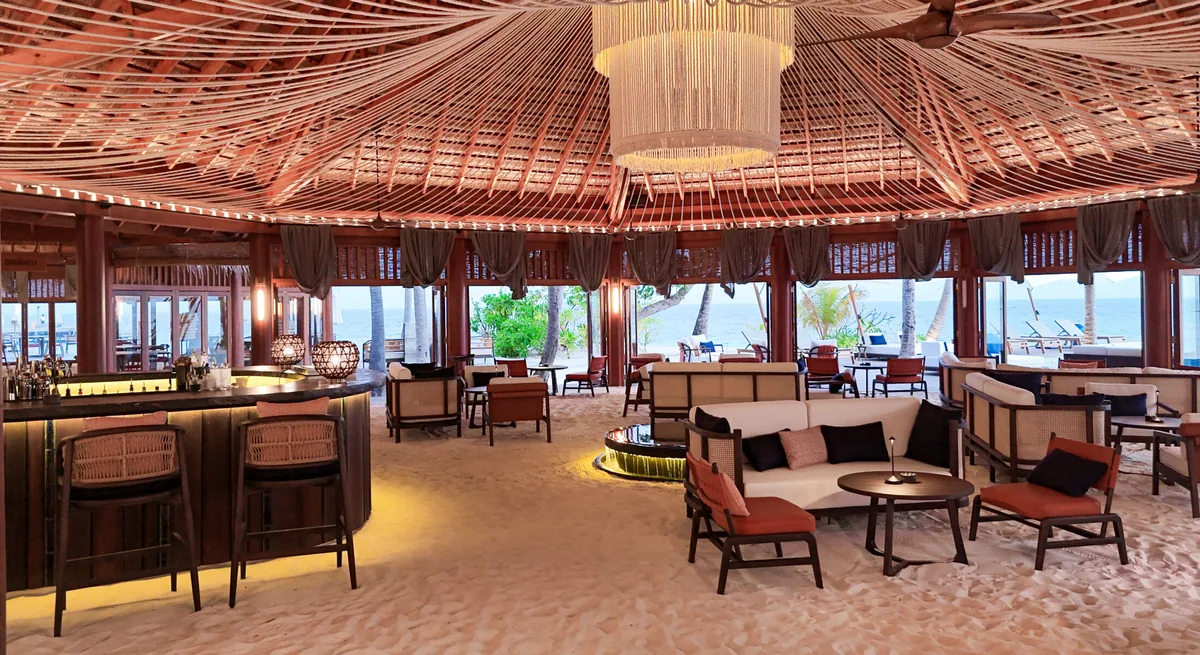 Mirihi Island Resort, dining, Alif Dhaal (South Ari) Atoll, Maldives, Akoya beach pavilion bar and lounge with the radial-rib timber thatch ceiling, the crystal cascade chandelier at the apex, the curved dark-wood bar, and the property-signature feet-in-sand floor.