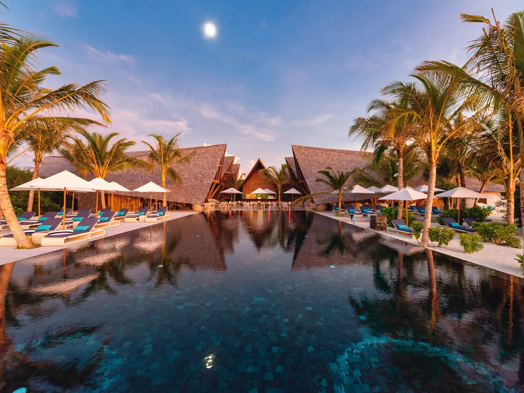 Mövenpick Resort Kuredhivaru, Latitude 5.5 angular pavilions reflected in dark-tile infinity pool at dusk, Noonu Atoll, Maldives